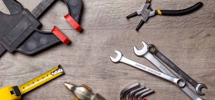 Verschiedene Werkzeuge wie Schraubenschlüssel, Zangen, Maßband und Klemme liegen auf einer Holzoberfläche, bereit für handwerkliche Arbeiten.