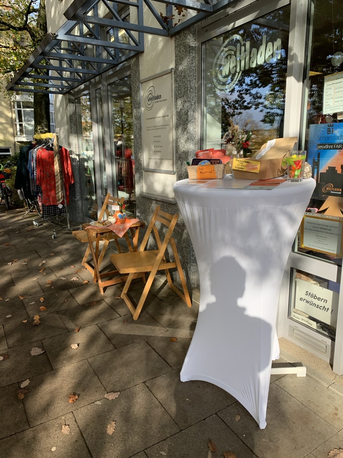 Foto mit Blick auf den Weltladen in Sennestadt. Vor dem Laden ist ein Stehtsich mit Waren